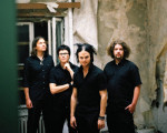 The Rasmus -bändin neljä mustiin pukeutunutta miesjäsentä seisoo rivissä rapautuneen seinän edustalla. Keskimmäisenä Lauri Ylönen, jolla mustat hiukset, joissa jakaus keskellä päätä.