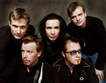 YUP-perheen promovalokuva vuodelta 2003. Kuvassan äkyy viisi muusikkoa, jotka poseeraavat tiukassa rykelmässä tummanruskeaa taustaa vasten. Jokaisella hepulla vakavat ilmeet kasvoilla. Keskimmäisenä mies, jolla pitkät mustat hiukset, muilla lyhyt letti.