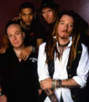 The Wildhearts -rokkibändin neljä miestä seisoo tummasävyisessä valokuvassa kahdessa rivissä. Oikeassa alakulmassa valkoiseen paitaan ja mustaan liiviin sonnustautunut rastapäinen heppu. Hänen vasemmalla puolellaan mustaan paitaan pukeutunut kalju mies. T