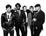Plain White T´s -bändin harmaasävyinen valokuva, jossa viisi muusikkoa seisoo vitivalkoista taustaa vasten rivissä. Kaikki ovat miehiä, yksi mustaihoinen. Osalla puvut yllään.