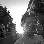 Harmaasävyinen valokuva Dark Filth Fraternity -nimisestä rokkibändistä, johon kuuluu neljä miestä. He seisovat ulkoilmassa siten, että auringonsäteet hohkavat miesten vierestä.