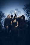 Tummasävyinen hämäräkuva Nightwish-bändin jäsenistä, jotka seisovat ulkoilmassa sinisen taivaan alla mustien puiden varjostaessa taustalla. Keskimmäisenä Anette, jolla hihaton musta paita, missä avara kaula–aukko.