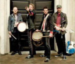 Coldplayn sakki seisoo mustan kaksiovisen puuoven edessä ulkoilmasa. Jäseniä kuvasas neljä kappaletta. He ovat kaikki lyhythiuksisia miehiä, joilla tummaa vaatetta yllään ja rumpuja sekä muita instrumentteja mukanaan.