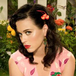 Lähipotretti ruskeahiuksisesta Katy Perrystä, jolla värikäs leninki yllään ja punatut huulet, sekä alta kulmien katsova katse. Taustalla vihreälehtisiä värikkäitä kukkia.