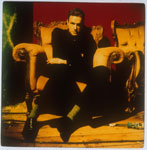 Vanhahtava valokuva Nick Caven bändiin kuuluneesta Mike Harveysta. Miehellä musta puku yllään. Hän istuu ylellisessä nojatuolissa punaista taustaa vasten. Lattia kellertävä ja laudoitettu.
