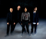 Neljä Red Hot Chili Peppers -bändin miestä seisoo rivissä mustaa taustaa vasten. Lattia (tai maa) on paksun vaalean sumukerroksen peitossa. Miesten vaatetuksen päävärinä musta.