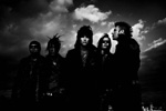 Hyvin tumma ja harmaasävyinen valokuva The 69 Eyesin kokoonpanoon kuuluvista muusikoista. He seisovat rivissä mustiin pukeutuneina pilvitaivaan alla. Osalla miehistä pitkät hiukset, osalla perustukka.