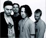 Harmaasävyinen valokuva Jack In The Box -bändin kokoonpanoon kuuluvista neljästä miespuolisesta jäsenestä, jotka seisovat tiiviinä rykelmänä vaaleata taustaa vasten. Keskimmäisellä miehellä puolipitkä musta tukka ja vasemman laidan miehellä jonkinlainen m